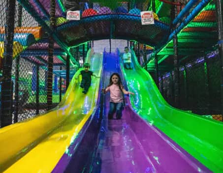 Children using the multi-level indoor playground slides at Rebounderz Grand Rapids.