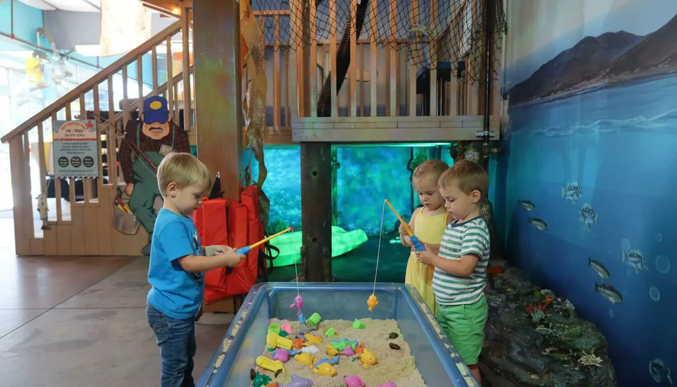 Young children exploring the coastal pier exhibit with a fishing-themed sensory bin at CRR Discovery Museum.