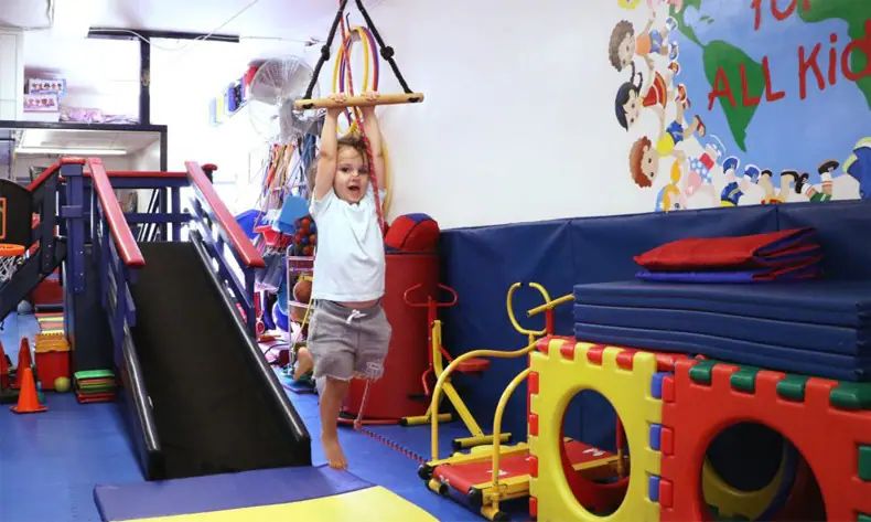 Child using suspended equipment beside padded ramps and soft-play pieces.