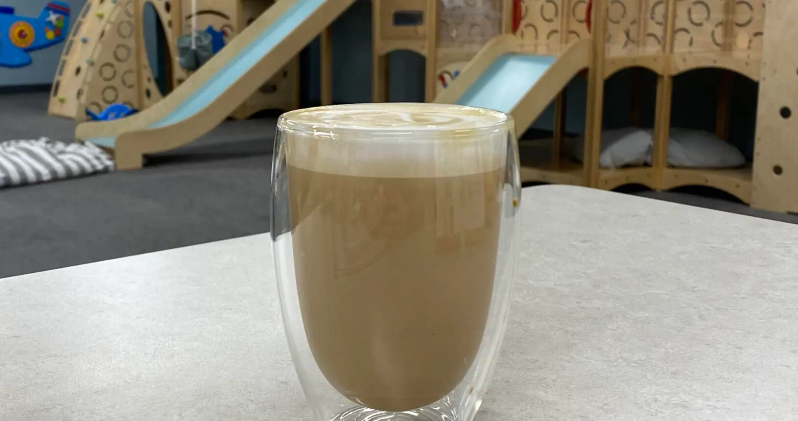 Coffee on a café table with Bug & Goose play structures visible behind it.