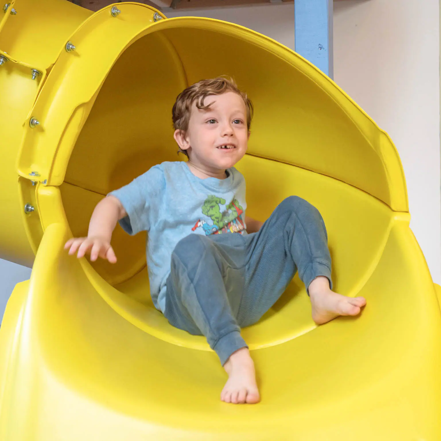 Young child sitting at the top of the yellow slide inside Kith + Kin