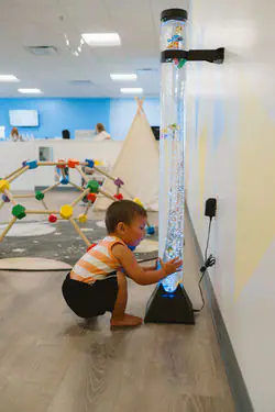 Child exploring a bubble tube sensory feature at To The Stars Play Cafe.