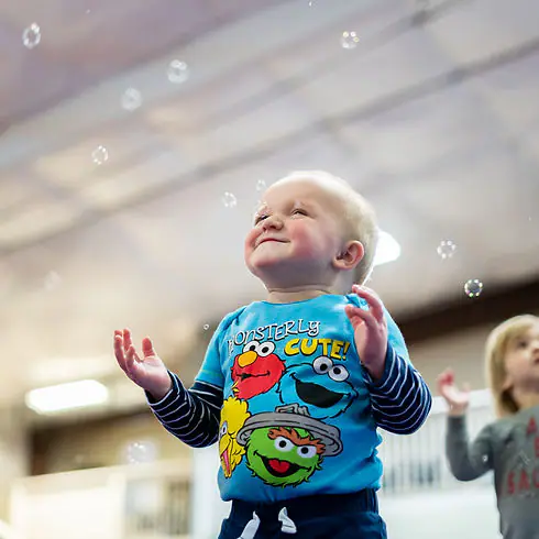 A toddler reaching for bubbles during a Roots play session.