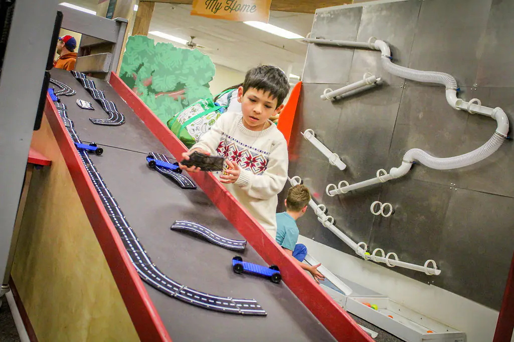 Child exploring a ramp-and-tube activity exhibit at Gallup Children's Museum.