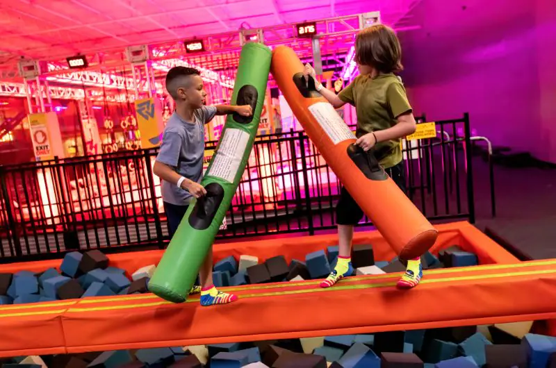 Two children playing on foam-battle beams inside Urban Air.