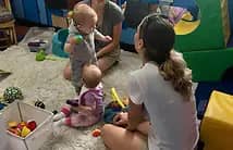 Babies and caregivers gathered in a soft floor-play area at Imagination Station.