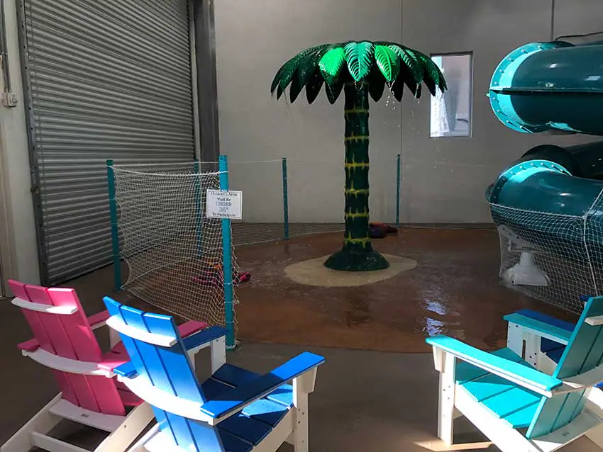 Smaller water-play area with seating near a palm-tree feature inside Splash Shack.