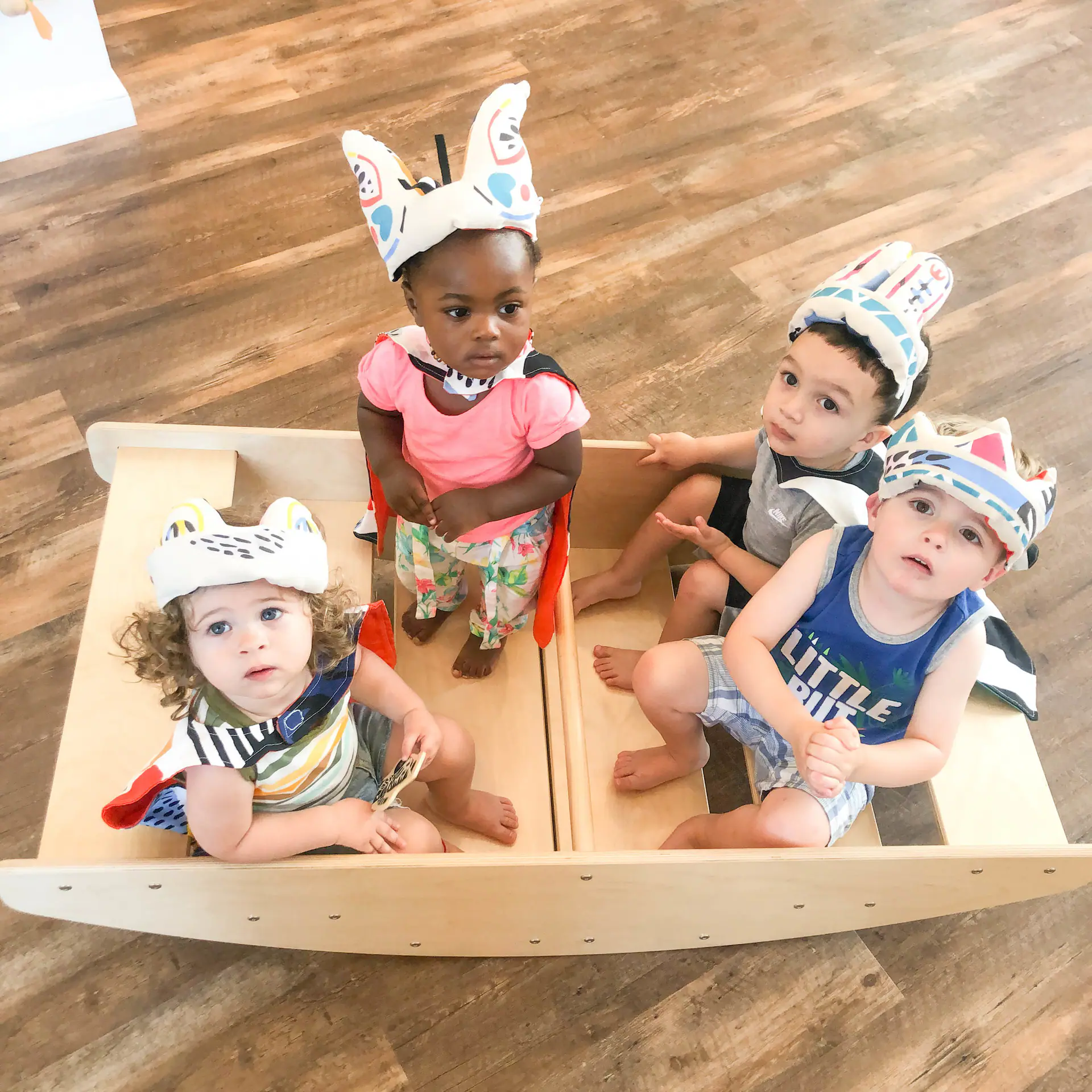 Four toddlers sitting in a wooden boat play feature at Kith + Kin