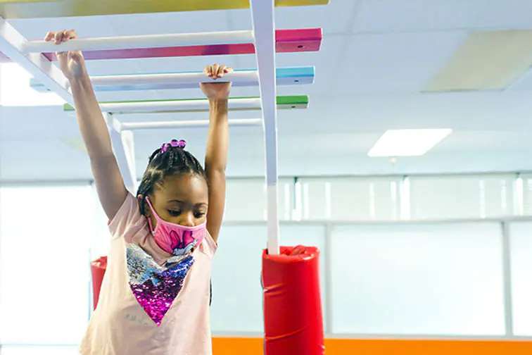 Child using overhead monkey-bar-style sensory equipment at The Sensory Spot.