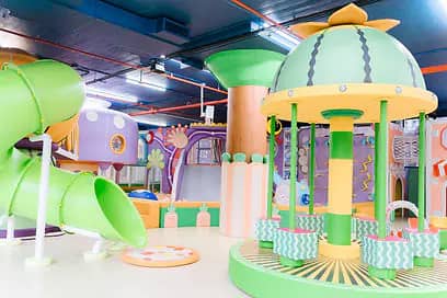 PeekabooO 21st Street themed play area with a carousel-style structure, pastel climbing elements, and a green tube slide.