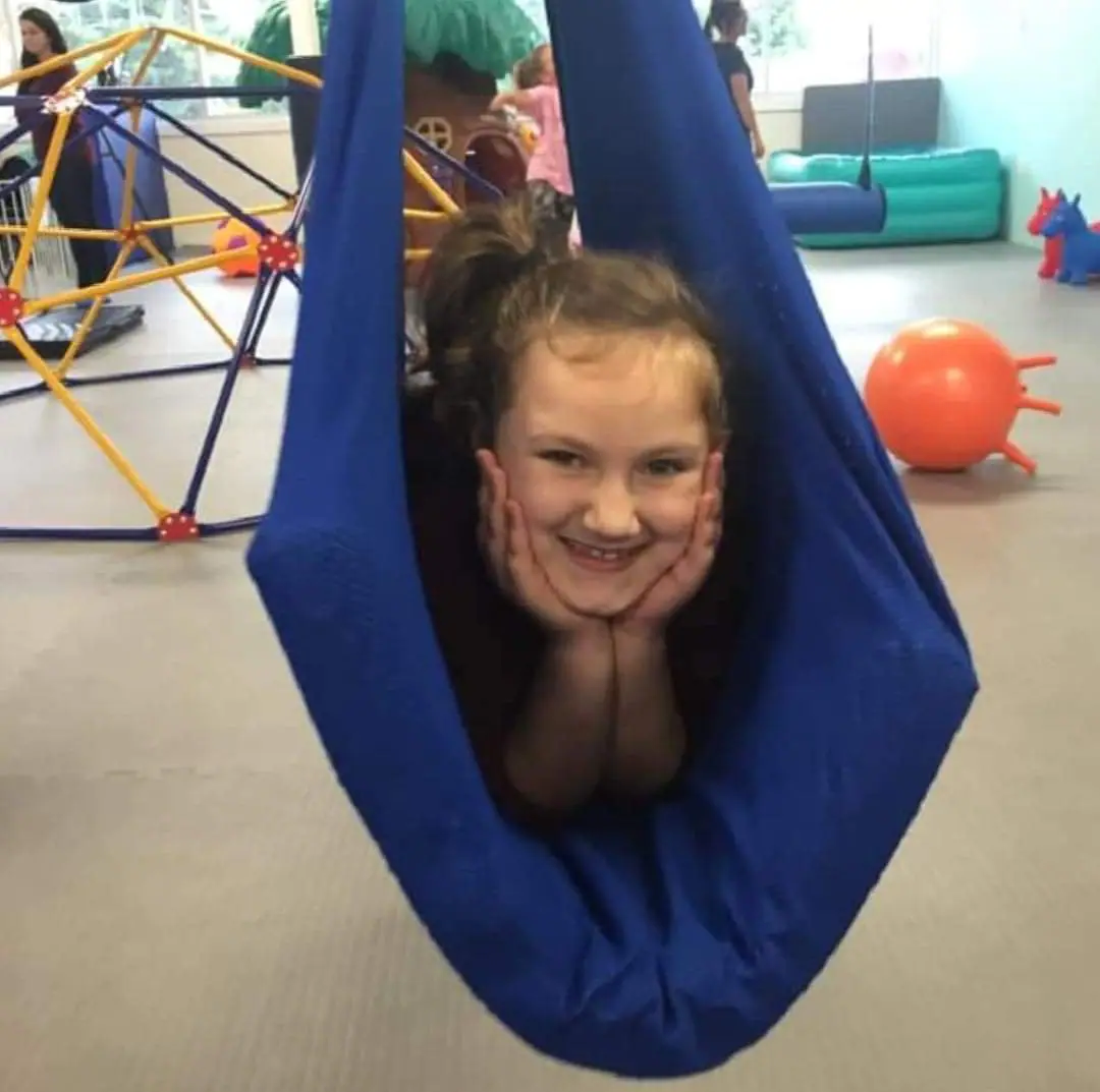 Child relaxing in a fabric sensory swing inside Chautauqua Children's Gym in Dunkirk.