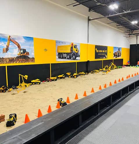 Diggers and trucks set up inside The Kids Dig It sandbox.