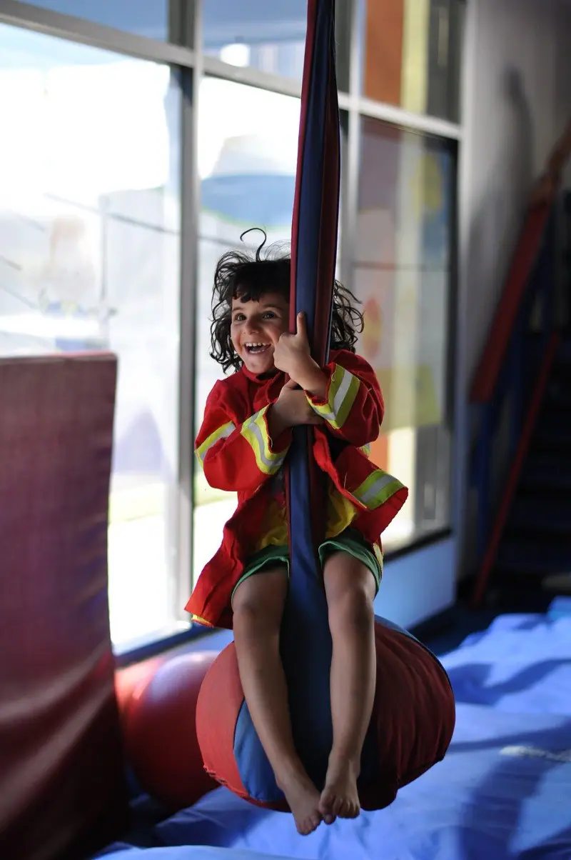 Child playing on adaptive indoor gym equipment at We Rock the Spectrum Kid's Gym in Morrisville.